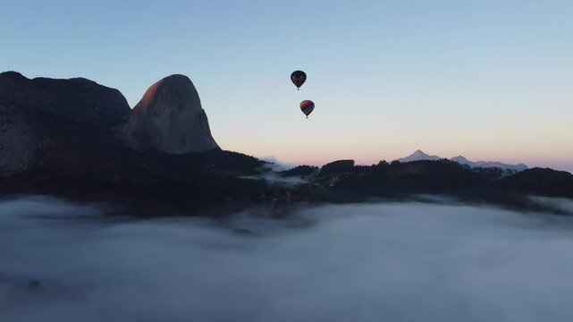 Dois bal&otilde;es de ar quente voando em frente &agrave; Pedra Azul durante a alvorada, com neblina no primeiro plano e o pico do Forno Grande ao fundo. Domingos Martins, Esp&iacute;rito Santo Brasil.