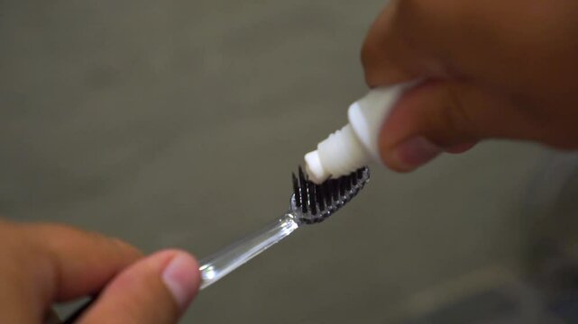 Close up of a hand putting toothpaste on the toothbrush in the bathroom. Oral cleaning concept.