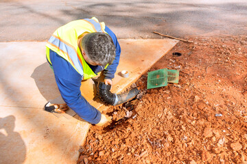 Worker wearing safety vest is crouched down, fixing drainage pipe in residential neighborhood at...