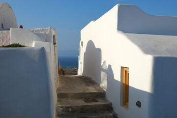 Santorini- tiny alleyway between lime-washed traditional houses with view of the mediterranean sea in the distance