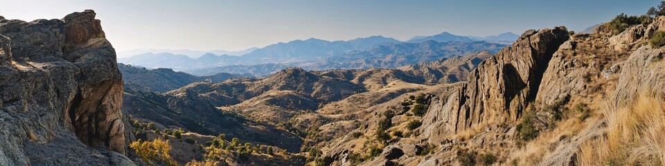 2410_096.narrow mountain trail hugging steep cliffside, rugged rocky terrain, layered sedimentary rock formations, sweeping valley views, sparse vegetation, distant mountain peaks