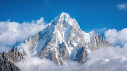 Obraz premium Majestic Snow-Capped Mountain Peak Surrounded by Clouds Under Bright Blue Sky, Capturing the Beauty of Nature and Stunning Alpine Scenery in Awe-Inspiring Landscape