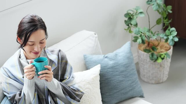 女性、飲む、寒い、冬、暖かい、コーヒー、笑顔、日本人、暖冬、対策、防寒、ストール、ショール、ブランケット、コピースペース、インテリア、リビングルーム、ライフスタイル、おしゃれ、リラックス、ほっこり、安心、ソファー、若い、寒暖差、紅茶、カップ、暖房、エアコン、マフラー、ポジティブ、快適、節電、室内、明るい、省エネ、爽やか、毛布、シンプル、キレイめ、きれいめ、寒さ、寒気、冷気、住宅、俯瞰、ハイアングル