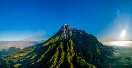 Aerial panoramic view of Mount Merapi, an active volcano in Central Java, Indonesia. Captured in the morning light with lush tropical forest and dramatic ridges. Drone photography