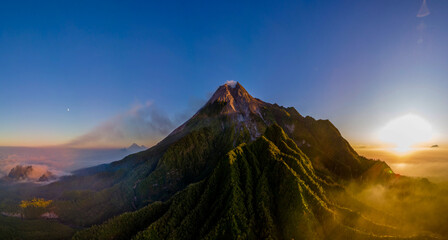 Aerial panoramic view of Mount Merapi, an active volcano in Central Java, Indonesia. Captured in the morning light with lush tropical forest and dramatic ridges. Drone photography