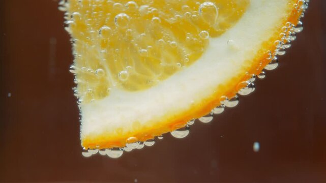 Close up of an orange slice in sparkling water with air bubbles. Slow motion, macro. 