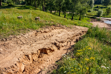 Gully in the ground on a slope, ravine formation in sandy soil, rain erosion