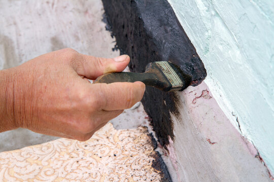 Painting the foundation of the house with mastic for waterproofing. Do-it-yourself home renovation.