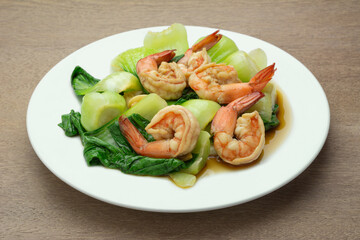 close up view of stir fried bok choy and shrimp with soy sauce in a ceramic dish on wooden table. asian homemade style food concept.