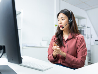 Confident Asian female call center agent with headset talking to client support for customer care in office. Asian woman telemarketing agent working on computer for consulting, customer support.
