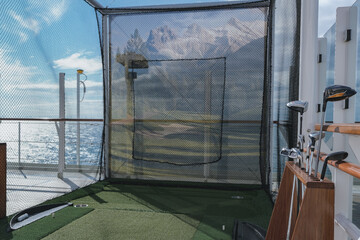 Golf tee shot simulator on outdoor sports deck of modern luxury ocean liner cruiseship cruise ship with net and golf clubs