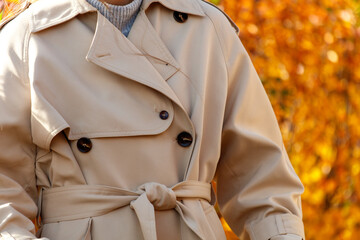 A woman wearing a tan trench coat with a white knit sweater