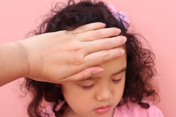 Fototapeta premium Mother's hand holding the forehead of her Asian toddler girl who has a fever to check her body temperature because she has a fever looks closely.