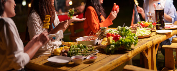 Group of young Asian friends enjoying dinner party together Barbecue grilling, drinking beer, people, food, healthy fruits and vegetables, celebrating, lifestyle drinks. New Year celebration concept.