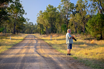 Fototapeta premium Senior man with camera on dirt road, rural landscape, wildlife bird photography hobby, retirement retiree activity pastime 