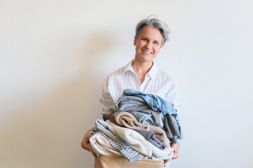 Gray haired mature woman with pile of clothes in basket isolated on white advertising banner