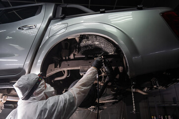 An auto mechanic applies anti-corrosion mastic to the underbody of a car.