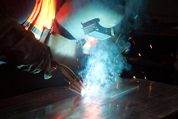 Welder uses torch to make sparks during manufacture of metal equipment, industrial professional worker