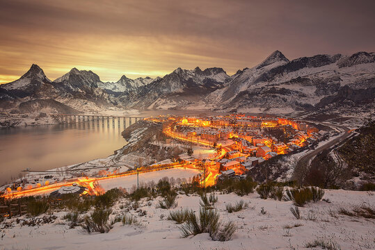 View of the town of Ria&ntilde;o, Leon, covered in snow at sunset with the reservoir and mountains in the background