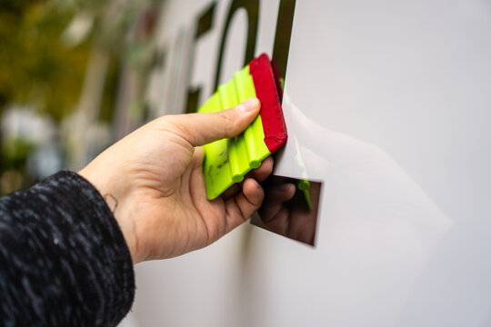 A person installing foil stickers on a car. Applying the sticker with a plastic spatula.