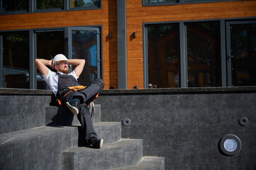 Construction worker relaxing near empty swimming pool. Builder in uniform has a break sitting in...