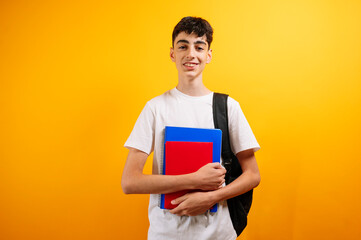 Teenage boy student holding books, yellow background.