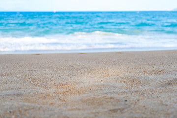 Close-up view of a sandy beach with a blurred turquoise sea in the background. The central part of the image is perfect for placing objects or text. A great choice for advertising materials