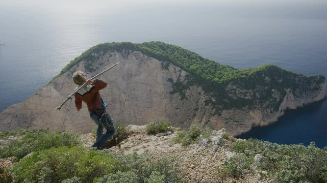 Cinematic wide shot of man tossing stick with rope over Greece cliffside then pulling it back up
