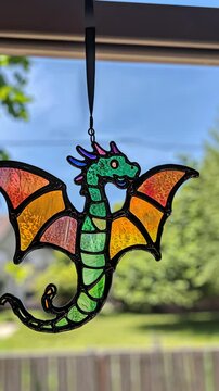 A charming stained glass dragon suncatcher is suspended from a window