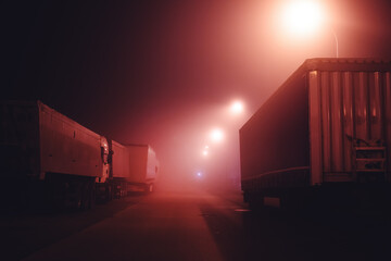 Semi truck parking lot with vehicles and trailers in foggy night