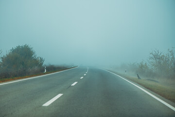 Empty countryside road covered in fog in cold autumn morning, bad weather conditions for driving