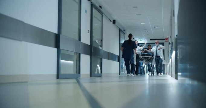 Urgent Scene in a Modern Clinic as Paramedics and Doctors Wheel an Unconscious Patient to the Intensive Care Unit. Young Female Nurse Runs Down the Corridor To Help the Team. Low Angle Footage