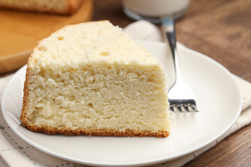 Piece of delicious sponge cake and fork on wooden table, closeup