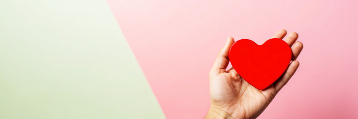 Obraz premium Hand Holding Red Heart on Pink and Green Pastel Background