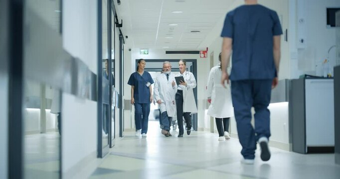 Cheerful Healthcare Team Moving Through a Spacious Hospital Corridor, Preparing for Their Next Shift while Having a Casual Conversation. Female Doctor, Surgeon and Senior Male Working in a Clinic