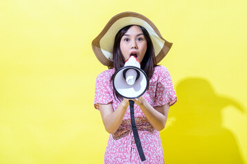 Asian woman wearing a straw hat and a pink floral dress, holding a megaphone with a surprised...
