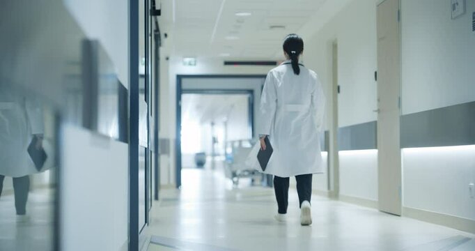 Female Doctor Walking Away in an Empty Hospital Hallway. General Practitioner Holding a Tablet Computer while Going to Intensive Care Unit or General Medicine Ward for Daily Patient Visit