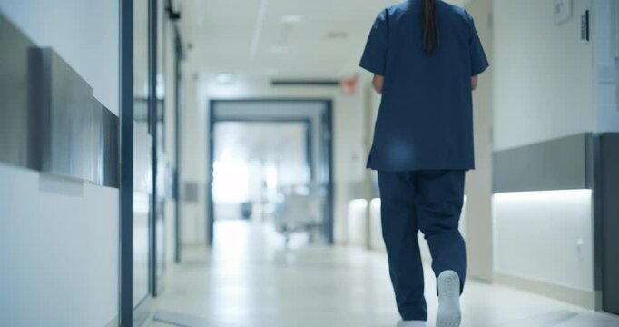Female Nurse Walking Away in an Empty Hospital Hallway. Surgeon Holding a Tablet Computer while Going to Operating Theater or General Medicine Ward for Daily Patient Visit