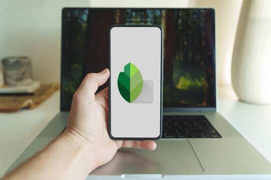 Snapseed photo editing application logo on smartphone screen in front of laptop