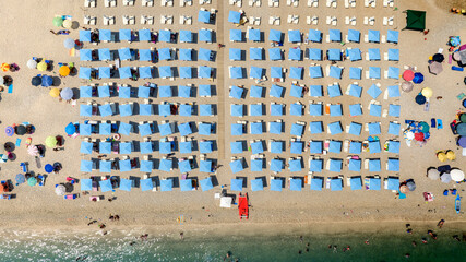 Aerial perpendicular view of a beach club with blue umbrellas in Puglia, Italy. The beach is sandy and crowded on this beautiful sunny summer day. Vacation on the Mediterranean Sea.