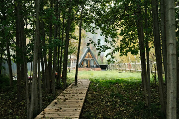 A-frame house in Scandinavian style. Landscape. Quiet rest. Glamping concept. Wooden house with a veranda in nature around the autumn forest.