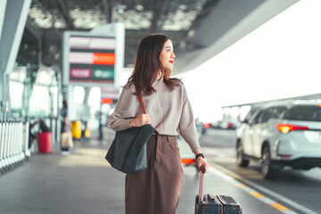 Standing tourist woman with travel luggage waiting at bus terminal for transport on day