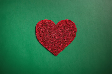 Obraz premium Red sparkle glitter heart on green background. Christmas and Valentines holiday