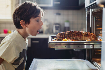 A young boy watches in amazement as a perfectly roasted dish is removed from the oven. The kitchen is warm and inviting, filled with delicious aromas and his anticipation.