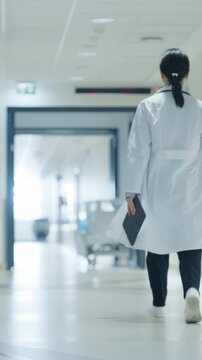 Vertical Screen: Doctor Walking Away in an Empty Hospital Hallway. General Practitioner Holding a Tablet Computer while Going to Intensive Care Unit or General Medicine Ward for Daily Patient Visit