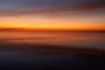 Long exposure abstract fine art photography of a red and orange sunset over the ocean. 