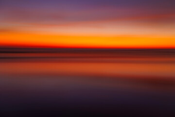 Long exposure abstract fine art photography of a red and orange sunset over the ocean. 