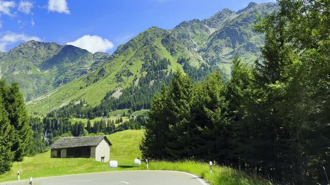 Car Point of View over Beautiful Mountain Road with swiss Alps and a Hut with Blue Sky and Clouds in a Sunny Summer Day in San Bernardino, Moesa, Grisons, Switzerland.