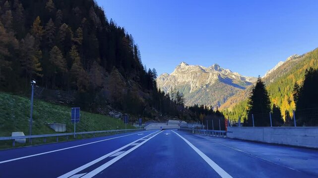 Car Point of View on Mountain Road and Tunnel with Trees in the Swiss Alps in Mountain Valley in a Sunny Autumn Day with Blue Sky in Sufers, Viamala, Grisons, Switzerland.