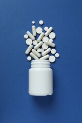 Various pills pouring out of a medicine bottle on color background